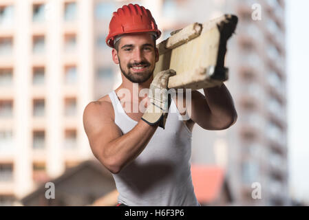 Smiling Carpenter Carrying A Large Wood Plank On His Shoulder Stock Photo