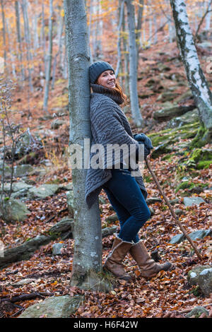 A glamourous woman hiking through the woods in autumn fall season wearing a casual wool poncho leisure wear woolly hat gloves Stock Photo