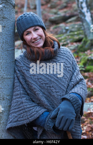 A glamourous woman hiking through the woods in autumn fall season wearing a casual wool poncho leisure wear woolly hat gloves Stock Photo