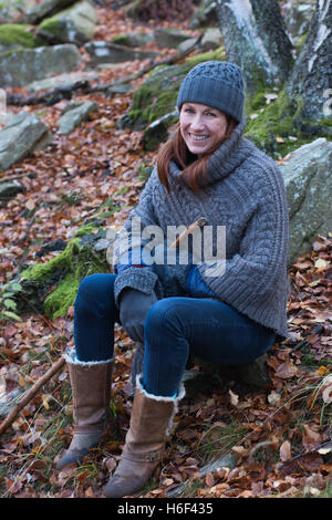 A glamourous woman hiking through the woods in autumn fall season wearing a casual wool poncho leisure wear woolly hat boots Stock Photo