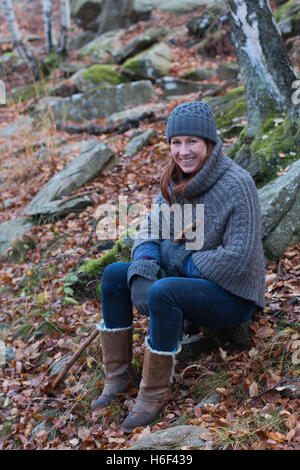 A glamourous woman hiking through the woods in autumn fall season wearing a casual wool poncho leisure wear woolly hat boots Stock Photo