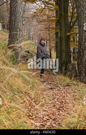 A glamourous woman hiking through the woods in autumn fall season wearing a casual wool poncho leisure wear woolly hat walking o Stock Photo