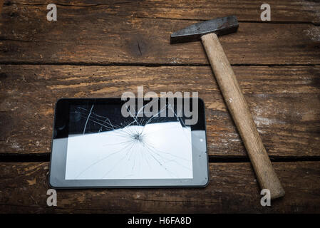 Hammer and tablet on the wooden table with broken glass. Stock Photo