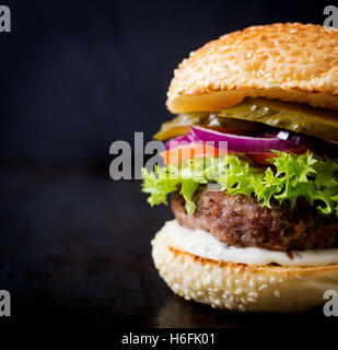 Big sandwich - hamburger burger with beef, pickles, tomato and tartar sauce on black background. Stock Photo