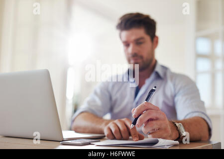Shot of young businessman at home office with laptop and taking notes. Focus on man hands holding pen. Stock Photo