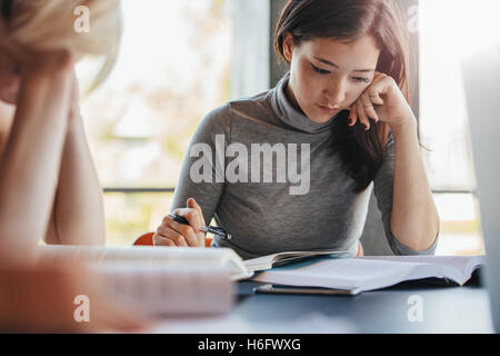 Young asian woman reading books with classmates studying around in university library. Students preparing hard for final exams. Stock Photo