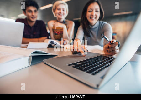Group of happy friends working on laptop in class. Female student with classmates studying together and looking at laptop comput Stock Photo