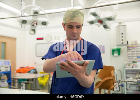A surgeon in a hospital operating theatre checks the patients' notes on his Ipad prior to an operation