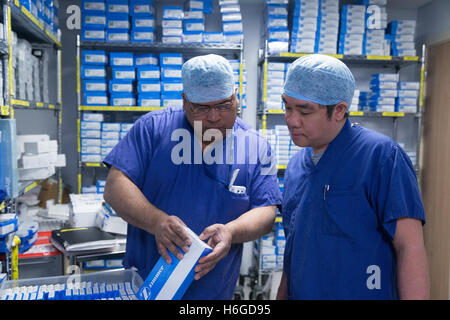 Two nurses in scrubs check medical equipment in the hospital storeroom including hip replacement sterile packs Stock Photo