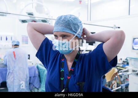 Female nurse tying her mask behind her head prior to an operation Stock Photo