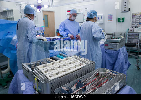 Medical staff in a hospital operating theatre during an knee replacement operation.Drills and equipment are in the foreground.