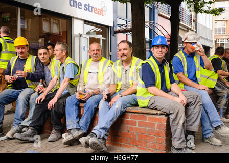 Builders wearing high visibility vests and hard hats take a tea break while working on shops. Stock Photo