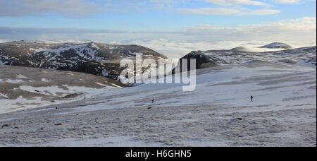Three skiers cross the Cairngorm plateau Scotland with snow covered mountains in the background. Stock Photo