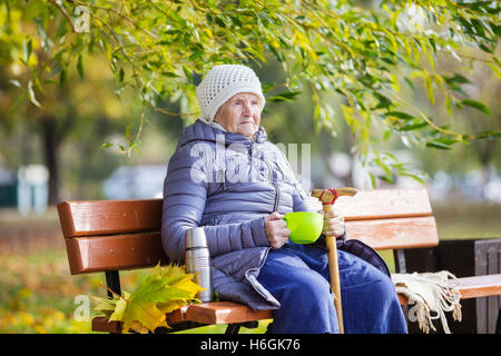 Senior woman drinking hot tea in autumn park Stock Photo