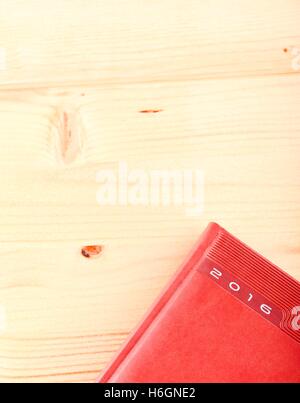 Vertical photo with top view on light wooden board with placed diary for year 2016. Diary is placed in a corner. Stock Photo