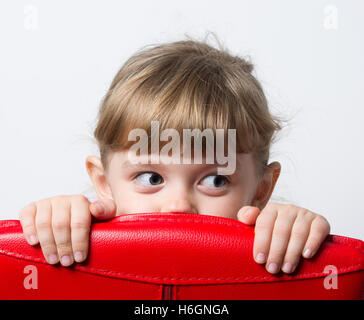 girl hiding behind the red chair Stock Photo