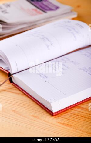 Vertical photo of opened diary with hand writing which is placed on light wooden board front of several newspapers which in back Stock Photo