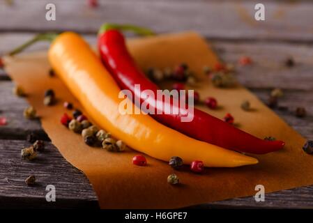 Horizontal photo of two chili peppers with yellow and red color which are placed on old worn wooden board with grey color. Veget Stock Photo