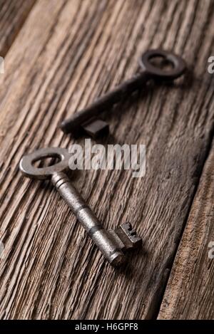 Vertical photo. Two old keys. Old keys placed on wooden board. Wooden board with worn surface. Dark photos. Board from planks. K Stock Photo