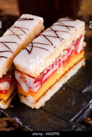 Vertical photo of two slices of sweet desert with color layers on sugar on the top placed on piece of black stone. Cup of coffee Stock Photo