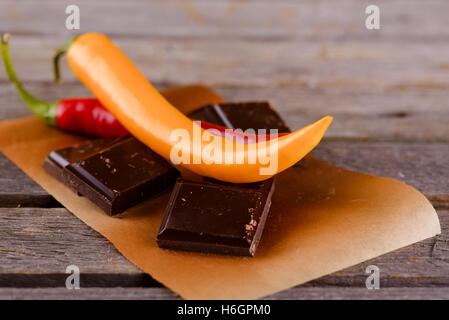Horizontal photo of two chili peppers red and yellow placed on pieces of dark chocolate. They are on paper sheet and old grey wo Stock Photo