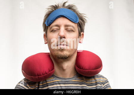 Bearded man with sleeping mask, red travel pillow and eyes closed on white background closeup Stock Photo