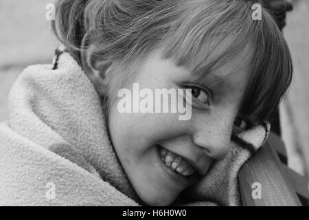 black and white portrait of little girl wrapped in blanket smiling at the camera with teeth showing Stock Photo