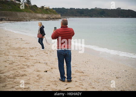 Man takes a photograph of a woman on Falmouth's Gyllyngvase Beach Stock Photo