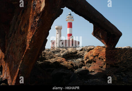 Fuerteventura, Canary Islands: El Toston Lighthouse, whose original structure was opened in 1897, seen through the rusty scrap of the wreck of a ship Stock Photo