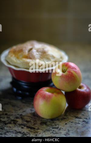 3 apples in front of a small pie in a red pie plate Stock Photo