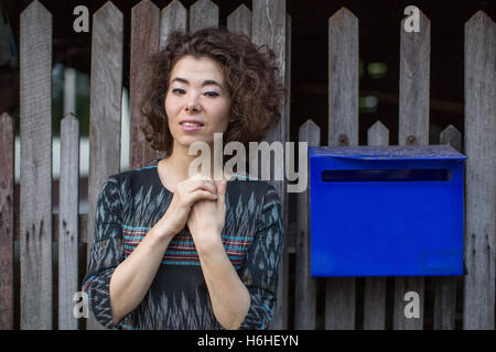 Young Asian woman standing in the street near the wooden fence with a mailbox. Stock Photo