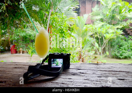 Orange juice frappe with camera dslr on wood table in garden Stock Photo