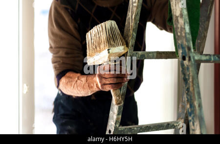 Painter on a ladder holding wall painting brush in his hand. Stock Photo