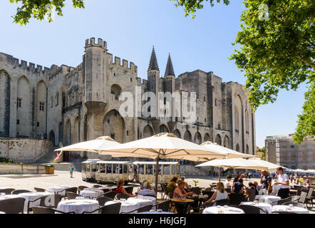 Restaurant overlooked by the Gothic twin towered facade of the Palais Neuf, Palais des Papes, Palace Square, Avignon, France Stock Photo