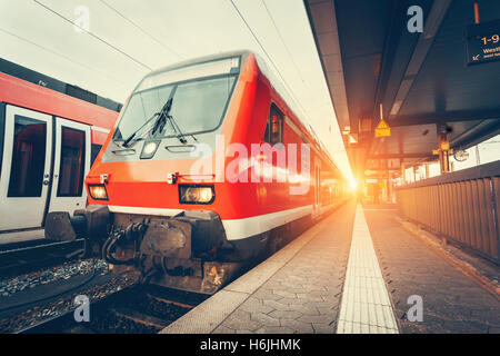 Modern high speed red commuter train at colorful sunset. Beautiful railway station. Railroad with vintage toning. Train at railw Stock Photo