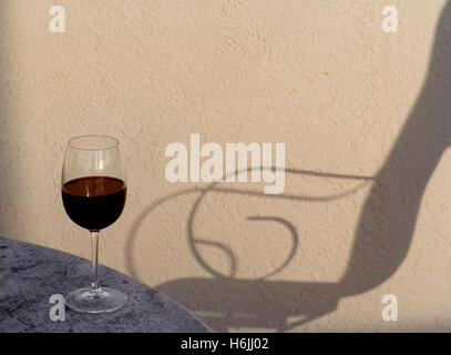 Classic red wine tasting glass on alfresco terrace table with shadow of lounger chair at sunset Stock Photo