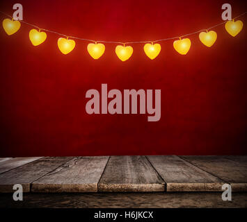 Hanging lights in heart shapes on rope with abstract empty red background .Empty wooden planks on background, ideal for product Stock Photo