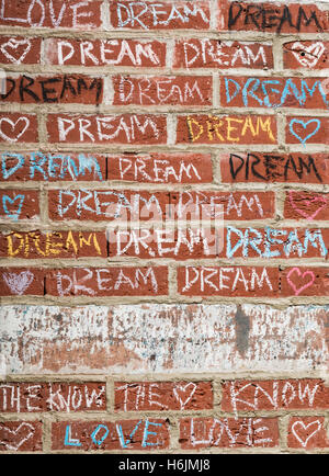 Coloured chalk graffiti on a red brick wall with the words love, dream, and the know on the outside of a shop. Stock Photo