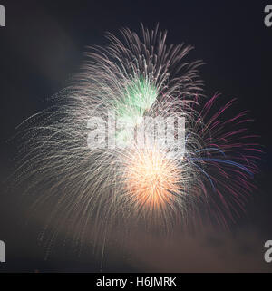Exploding fireworks in green, orange, red and blue in a smokey night sky Stock Photo