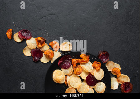 Vegetable chips on the black plate on the dark stone table Stock Photo