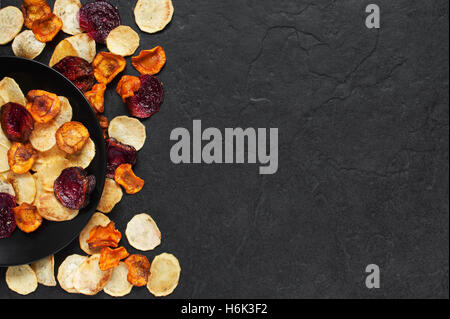 Vegetable chips on the black plate on the dark stone table Stock Photo