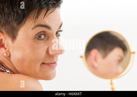 Closeup of a black-haired woman of middle age with round makeup mirror against white background to the page looking. Stock Photo