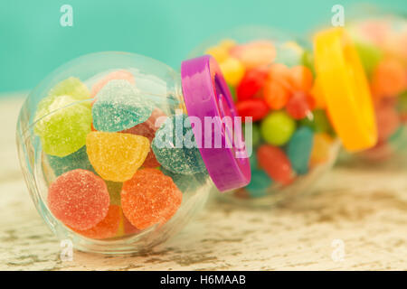 Three glass jars full of jellybeans on wooden table with blue background. Focus in the foreground Stock Photo