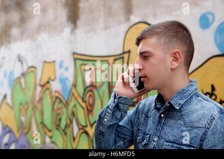 Young teenager with her cell phone and near of a wall painted with graffiti Stock Photo