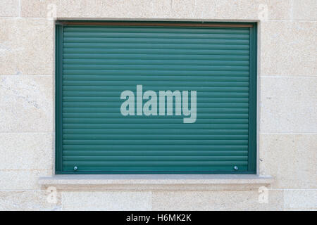 Green closed metal shutter on a window of a stone house Stock Photo