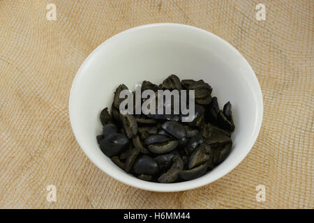 Sliced black olives in white bowl on burlap Stock Photo