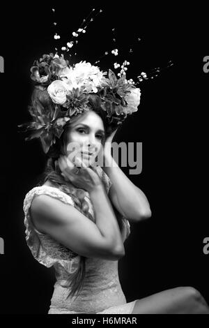 Model woman with architectural floral hair piece wearing white lace dress photoshoot against black studio backdrop, monochrome Stock Photo