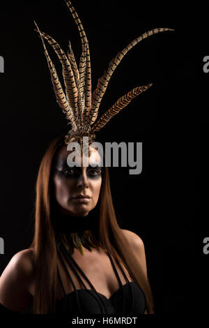 Tanned female model in amazonian superhero outfit with feather headdress, dramatic shadows Stock Photo