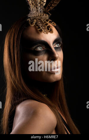 Tanned female model in amazonian superhero style outfit with feather headdress, dramatic shadows Stock Photo