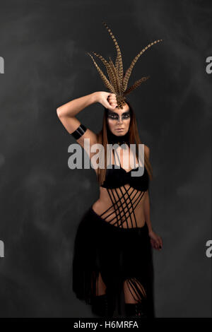 Tanned female model in amazonian superhero style outfit with feather headdress, smoky backdrop, smoke Stock Photo